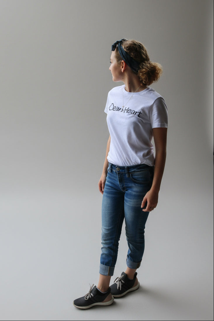 Person wearing a white t-shirt with 'Clean Heart' text, standing on a wooden deck overlooking a tropical beach.