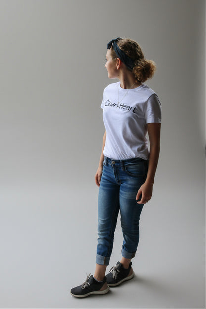 Person wearing a white t-shirt with 'Clean Heart' text, standing on a wooden deck overlooking a tropical beach.